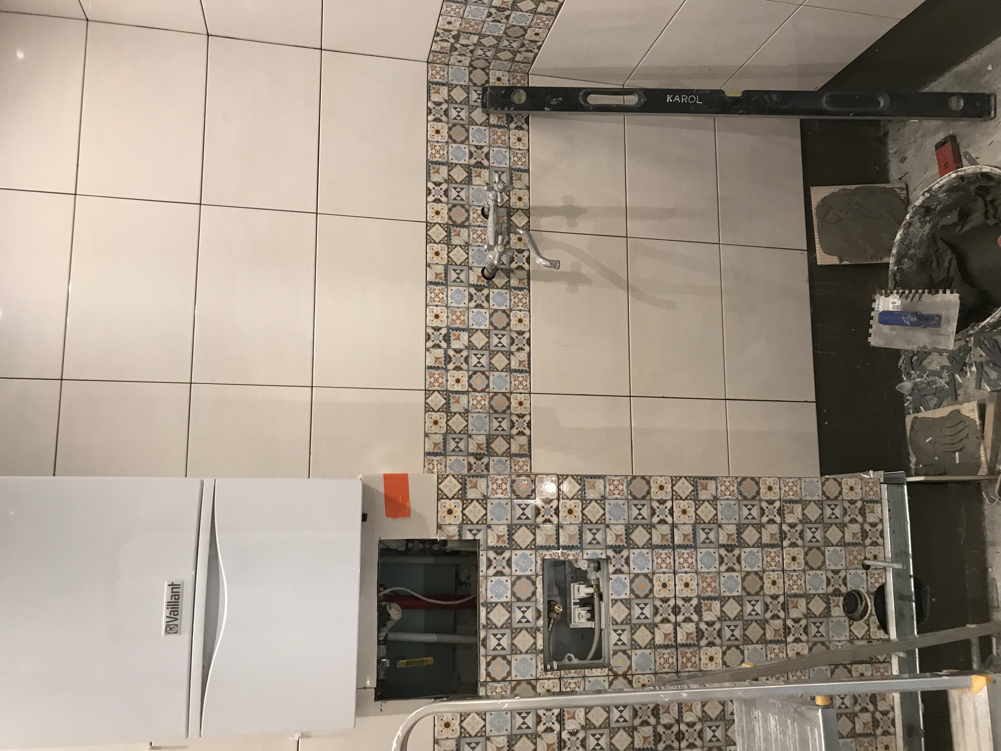 Montaż płytek wzorzystych w łazience, widoczny bojler Vaillant, poziomica Karola i narzędzia glazurnicze.