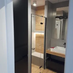 Nowoczesna łazienka z kabiną prysznicową typu walk-in, drewnopodobnymi płytkami i podświetleniem LED, widok z perspektywy wejścia.