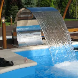 Nowoczesny basen z kaskadą wodną ze stali nierdzewnej, widoczne płetwy i drewniany taras.