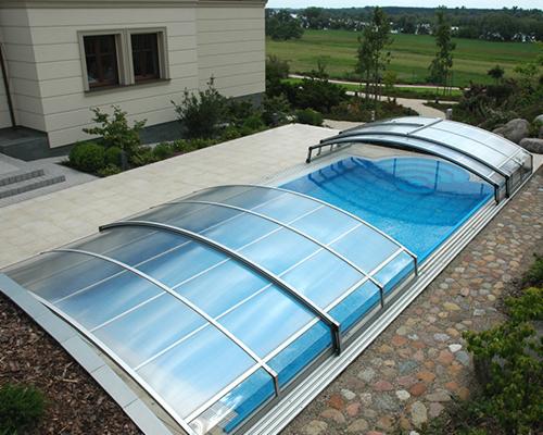 Zadaszony basen zewnętrzny z niebieską wodą, otoczony jasną kostką brukową i kamienną ścieżką, widok z góry.