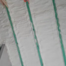 Ocieplenie poddasza pianką PUR, widoczne krokwie z zielonymi łatami i biała, równomiernie nałożona pianka.