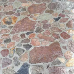 Kamienna nawierzchnia tarasu z nieregularnych, brązowo-szarych kamieni, po deszczu, z widocznymi smugami wody i fugami cementowymi.