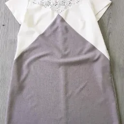 Krótka sukienka damska z koronkową górą i geometrycznym wzorem, wisząca na wieszaku na tle drewnianej powierzchni.