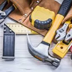 Zestaw narzędzi rzemieślniczych rozłożony na jasnych, drewnianych deskach: młotek z żółtym trzonkiem, miara zwijana, kątownik stolarski, obcęgi, kombinerki i inne narzędzia w skórzanym pasie...