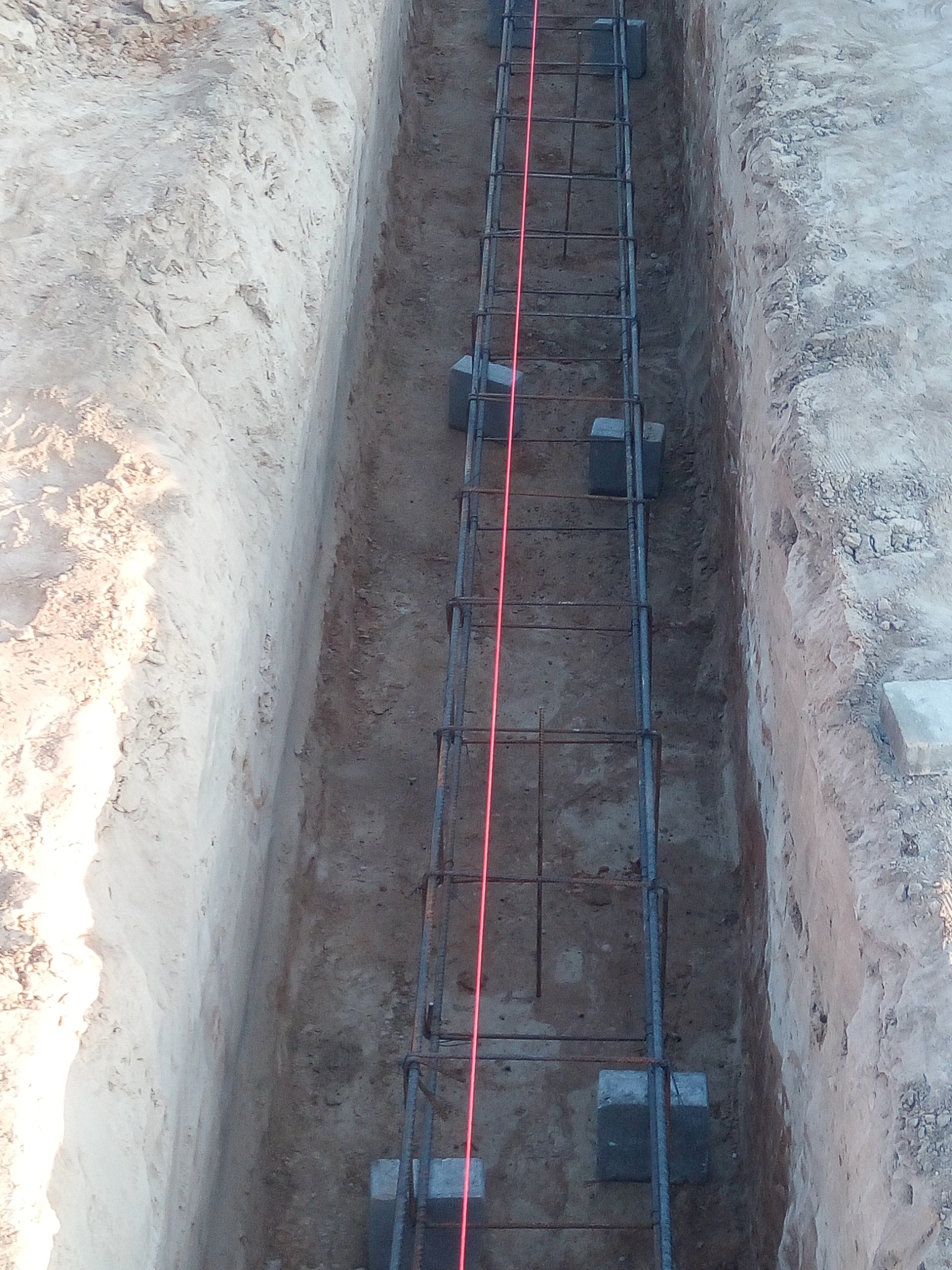 Wykop zbrojony stalowymi prętami i poziomowany laserowo, przygotowany pod wylewkę fundamentów, w ziemi o zróżnicowanej strukturze.