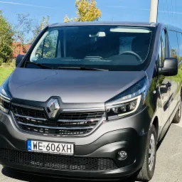 Szary bus Renault Trafic z polskimi tablicami rejestracyjnymi WE 606XH, zaparkowany na zewnątrz w słoneczny dzień.
