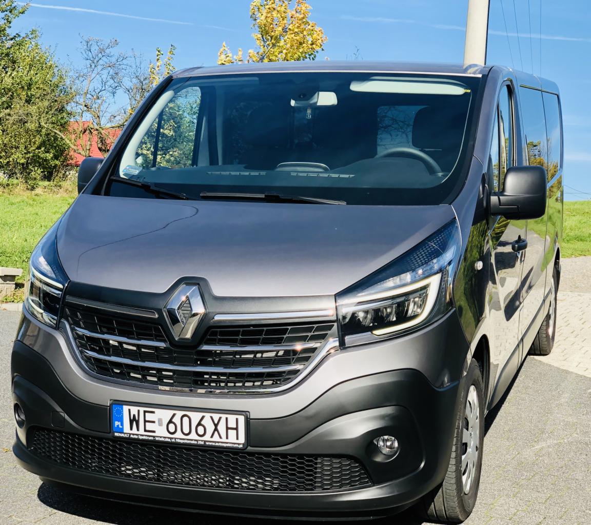 Szary bus Renault Trafic z polskimi tablicami rejestracyjnymi WE 606XH, zaparkowany na zewnątrz w słoneczny dzień.