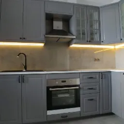 Szara kuchnia z oświetleniem LED pod szafkami, czarną armaturą i sprzętem AGD marki Samsung i Electrolux.