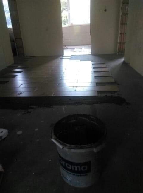 Fragment podłogi w trakcie układania płytek, widoczny częściowo ułożony wzór oraz wiadro z zaprawą w pierwszym planie.