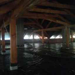 Przygotowanie poddasza do wylewki: rozłożona folia ochronna na izolacji, drewniane słupy podtrzymujące konstrukcję dachu, widoczne okna dachowe w tle.