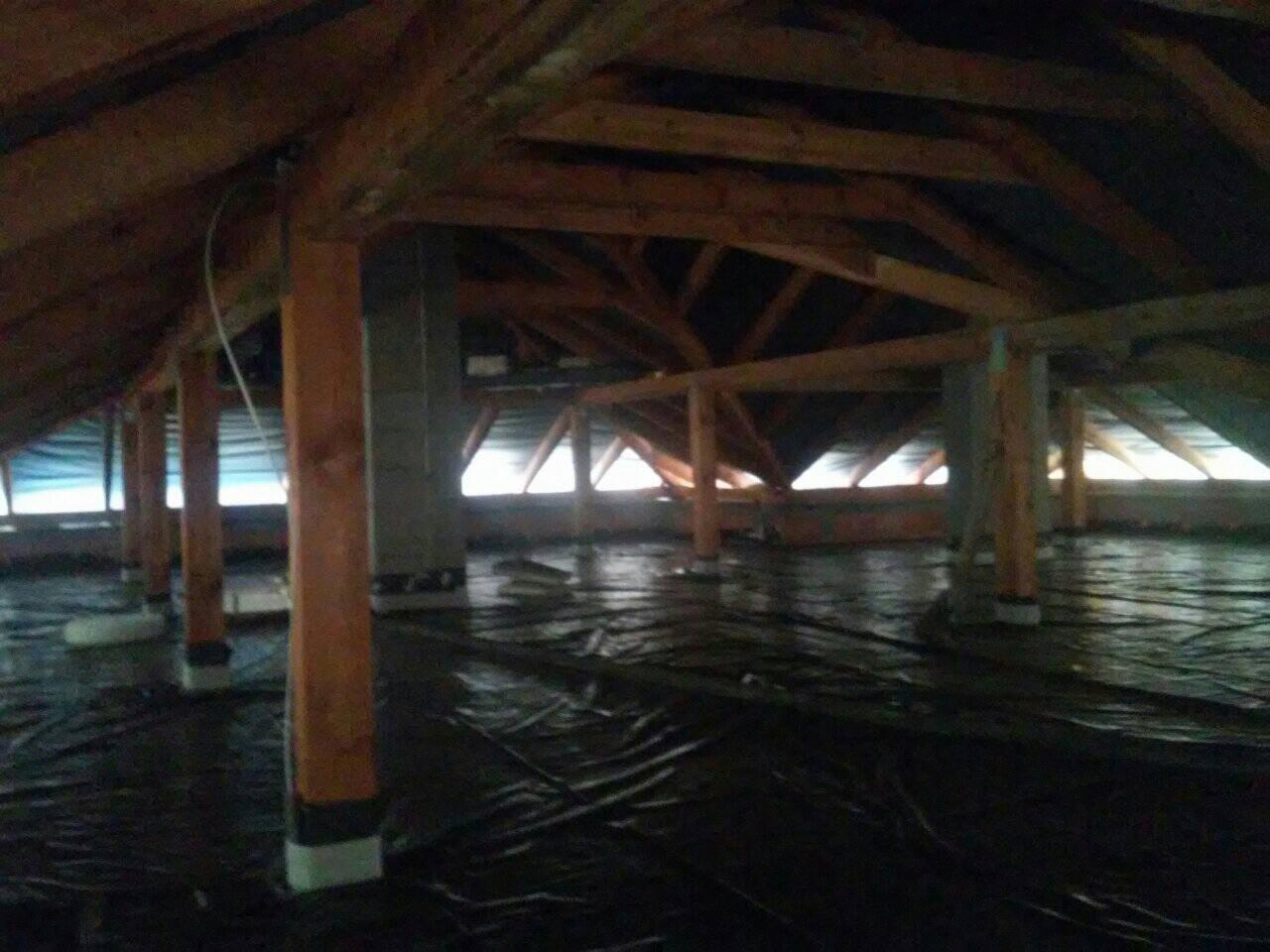 Przygotowanie poddasza do wylewki: rozłożona folia ochronna na izolacji, drewniane słupy podtrzymujące konstrukcję dachu, widoczne okna dachowe w tle.