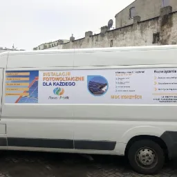 Biały samoch&oacute;d dostawczy z reklamą instalacji fotowoltaicznych firmy Power Profit, zaparkowany na tle miejskiego budynku.
