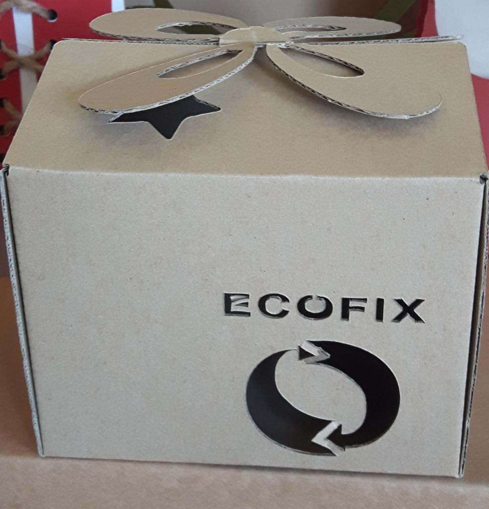 Kartonowe pudełko z wyciętym logo ECOFIX i symbolem recyklingu, ozdobione kokardą z tektury falistej.