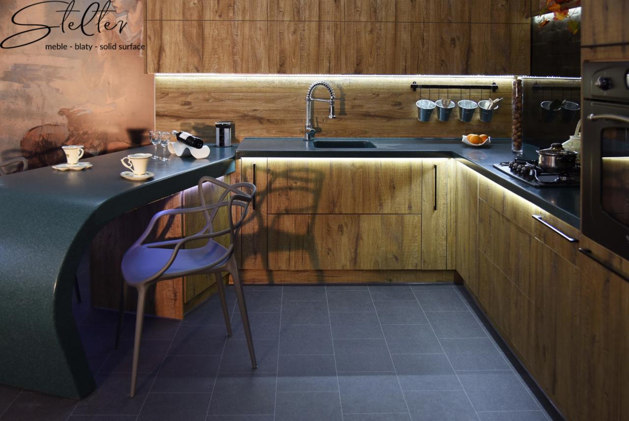 Nowoczesna kuchnia z drewnianymi frontami, podświetlanym blatem i barkiem z krzesłem, na blacie filiżanki i wino.