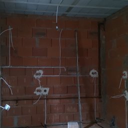VOLT-MAR MARCIN OGONOWSKI - Wewnętrzna ściana z czerwonej cegły z przewodami elektrycznymi, puszkami pod gniazdka i rurkami instalacyjnymi, surowy stan.