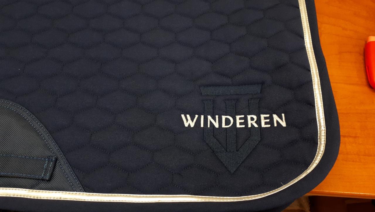 Granatowy czaprak jeździecki z pikowaniem w romby, srebrną lamówką i wyhaftowanym białym logo 'WINDEREN'.