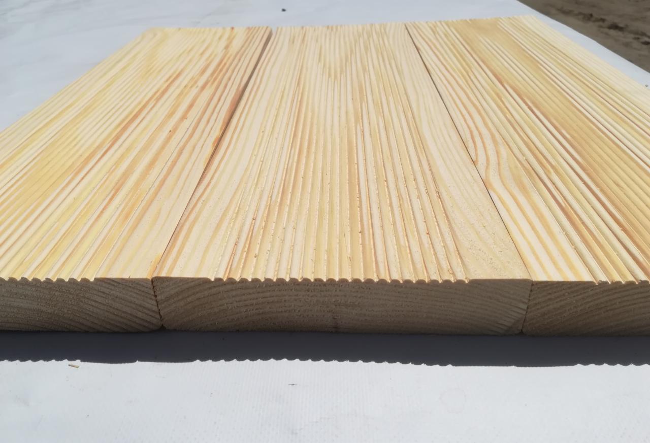 Bliski widok na trzy połączone deski z jasnego drewna z wyfrezowanymi krawędziami, ukazujące strukturę słojów.