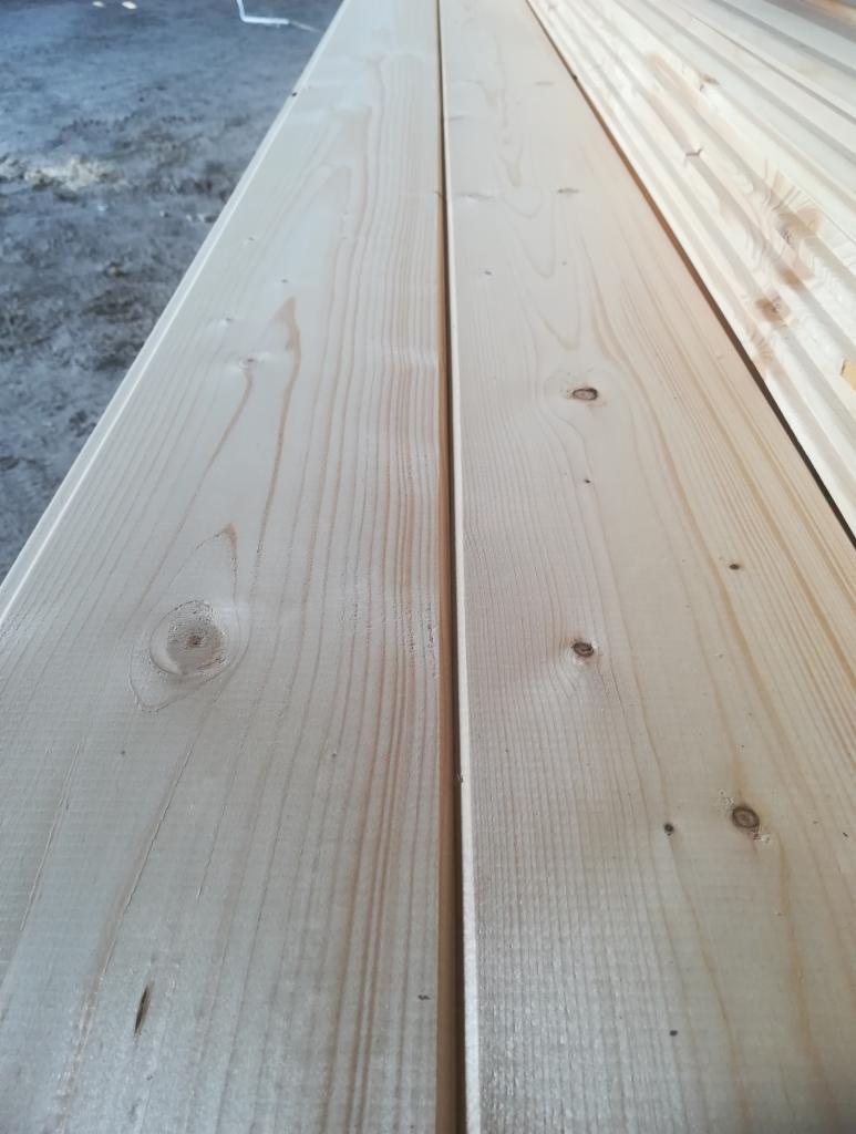 Przygotowane deski elewacyjne z widocznymi słojami drewna, gotowe do montażu w Topolnicy, z fragmentem deski profilowanej z prawej strony.