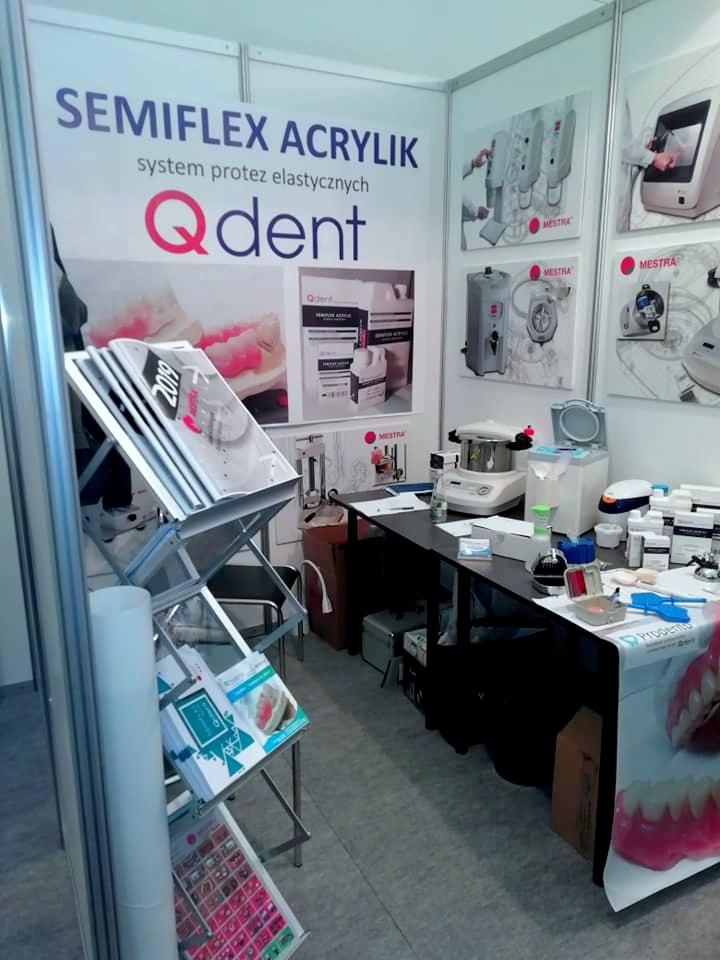 Stoisko targowe z materiałami i urządzeniami do wykonywania protez elastycznych Semiflex Acrylik, z widocznym logo Qdent, prezentujące proces wytwarzania i gotowe produkty.