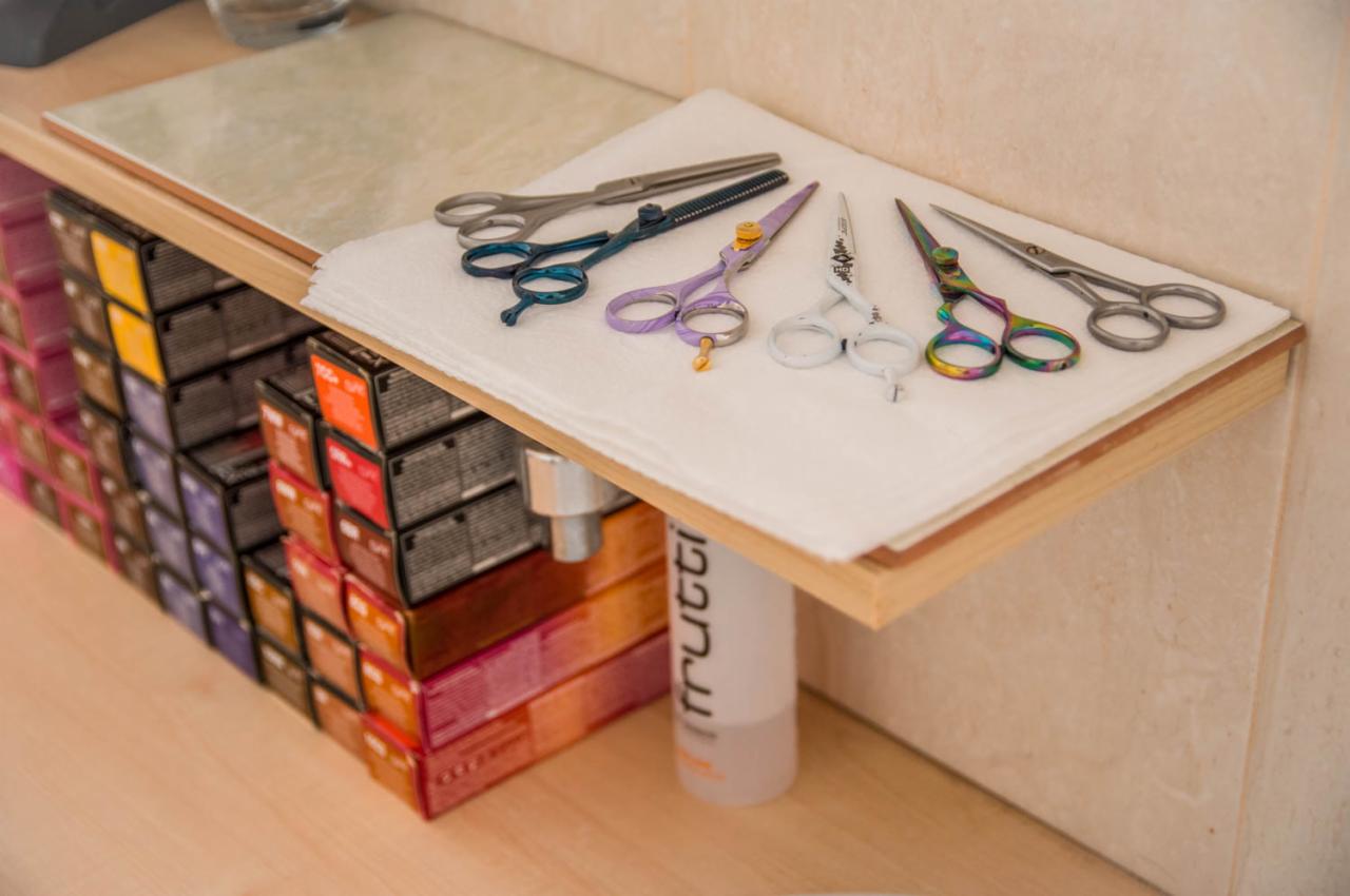 Różnorodne nożyczki fryzjerskie ułożone na białym ręczniku, obok pudełka farb do włosów i butelka kosmetyku.