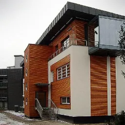 Nowoczesny budynek usługowy z drewnianą elewacją, przeszklonymi elementami i logo 'MOLO' na elewacji, widoczny z zewnątrz w pochmurny dzień.