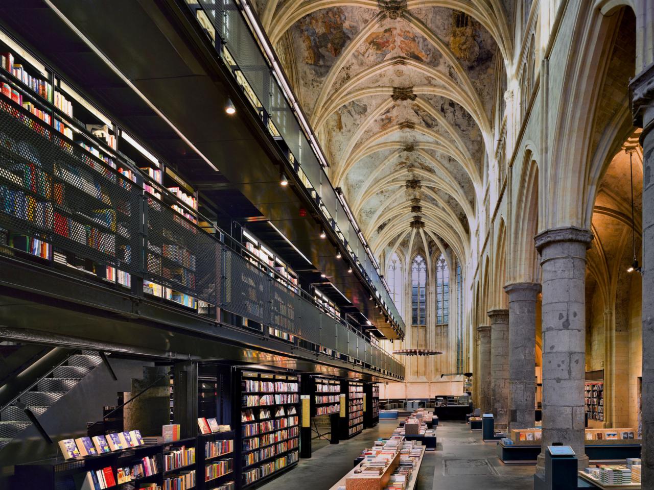 Księgarnia w dawnym kościele: wysokie sklepienie z malowidłami, regały z książkami na dwóch poziomach, stalowa konstrukcja antresoli, kamienne kolumny wzdłuż nawy, naturalne światło z okien