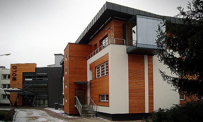 Nowoczesny budynek usługowy z drewnianą elewacją, przeszklonymi elementami i logo 'MOLO' na elewacji, widoczny z zewnątrz w pochmurny dzień.