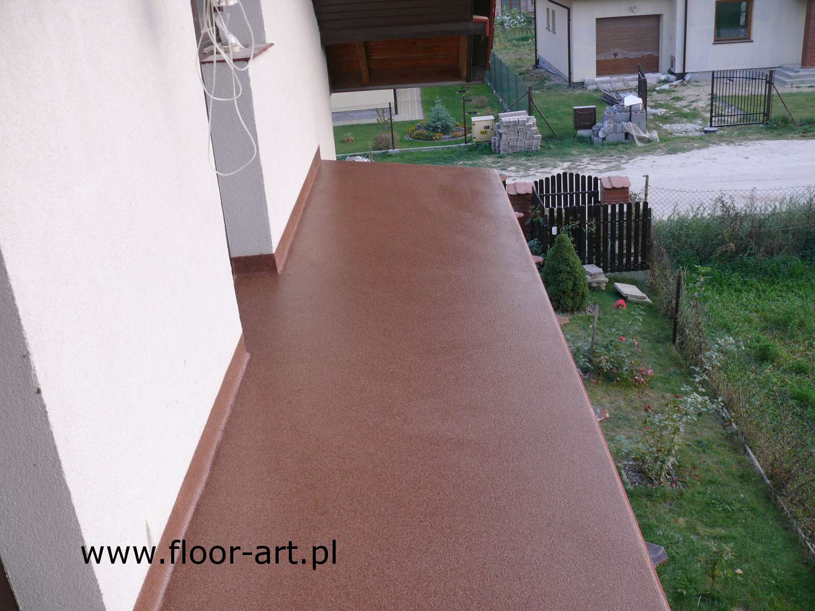 Balkon wykończony brązową posadzką żywiczną z widokiem na ogród, z widocznym adresem strony internetowej firmy.