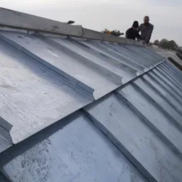 Montaż blachy na dachu z widocznymi dwoma dekarzami i narzędziami, z perspektywy dolnej krawędzi dachu.