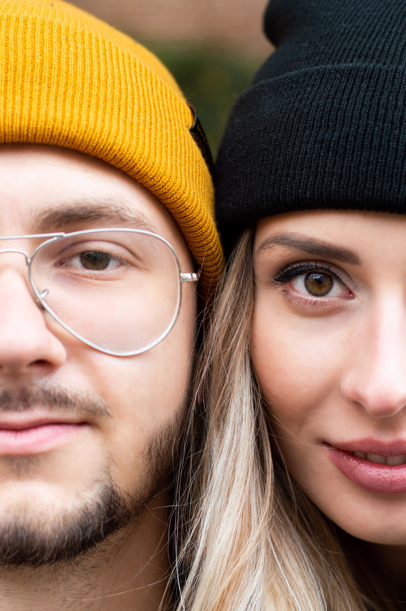 Portret zbliżeniowy pary: mężczyzna w żółtej czapce i okularach, kobieta w czarnej czapce, widoczne połówki twarzy, spojrzenie w obiektyw.