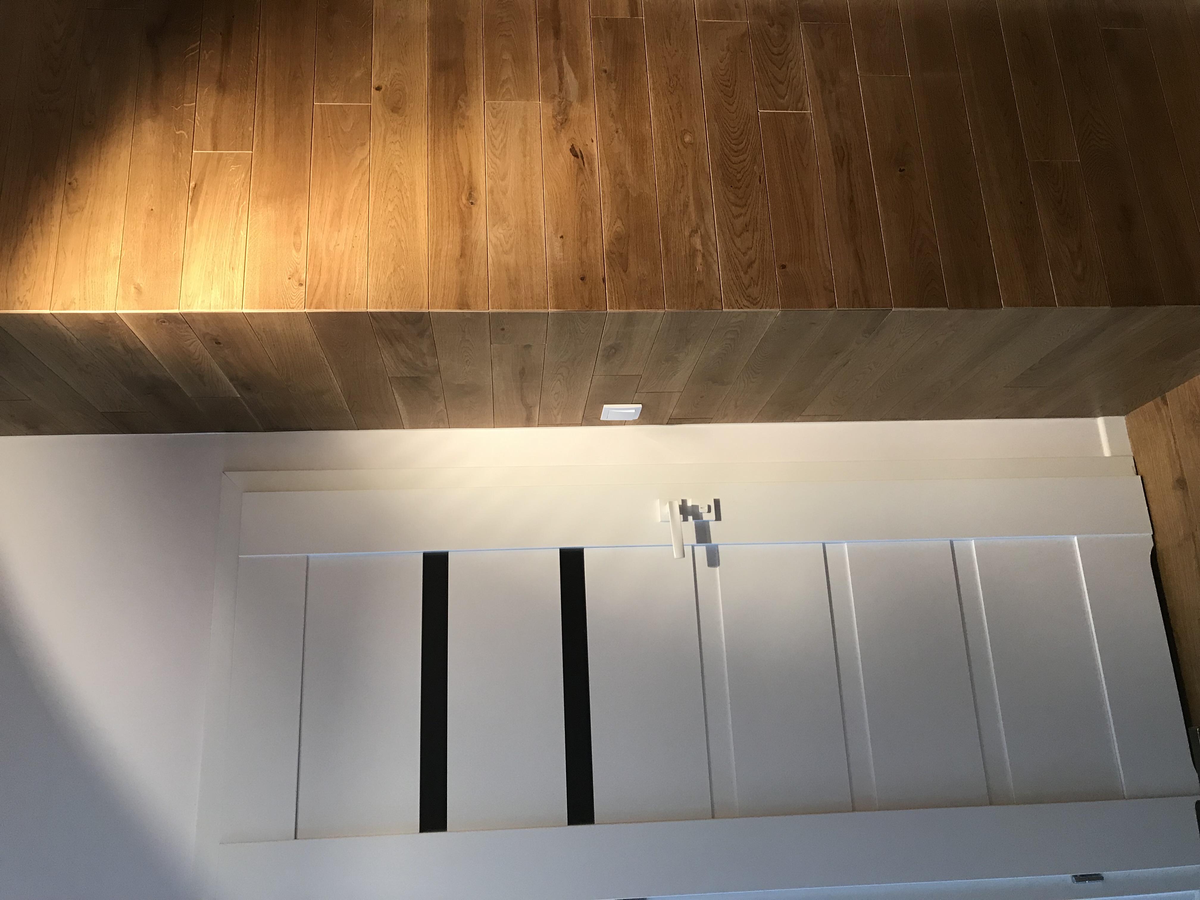 Nowoczesne, białe drzwi przesuwne z czarnymi wstawkami pod drewnianą podłogą ułożoną w jodełkę.