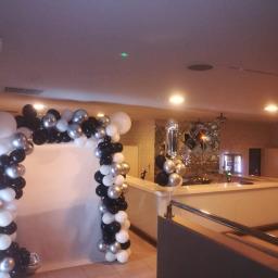 Odlotowy balon - Dekoracja balonowa w odcieniach czerni, bieli i srebra tworząca łuk wejściowy, z dodatkowymi balonami przy barze z lustrzaną ścianą w tle.