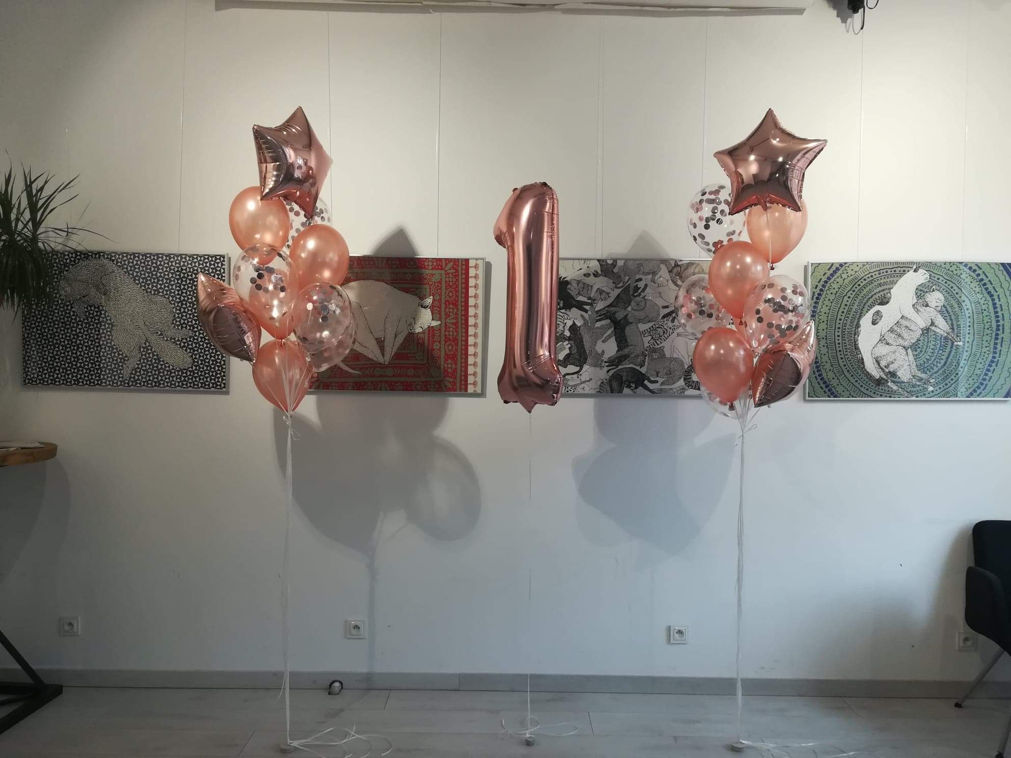 Dekoracja balonowa na pierwsze urodziny: dwa bukiety z różowych balonów, w tym balon w kształcie gwiazdy, oraz balon foliowy w kształcie cyfry 1, ustawione na tle białej ściany z trzema obrazami.