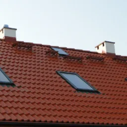 Czerwona dachówka ceramiczna na dachu skośnym z oknami dachowymi i dwoma kominami wentylacyjnymi.