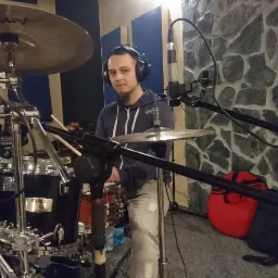 Perkusista z Czechowic-Dziedzic w słuchawkach, grający na perkusji w studiu nagraniowym z kamienną ścianą w tle.