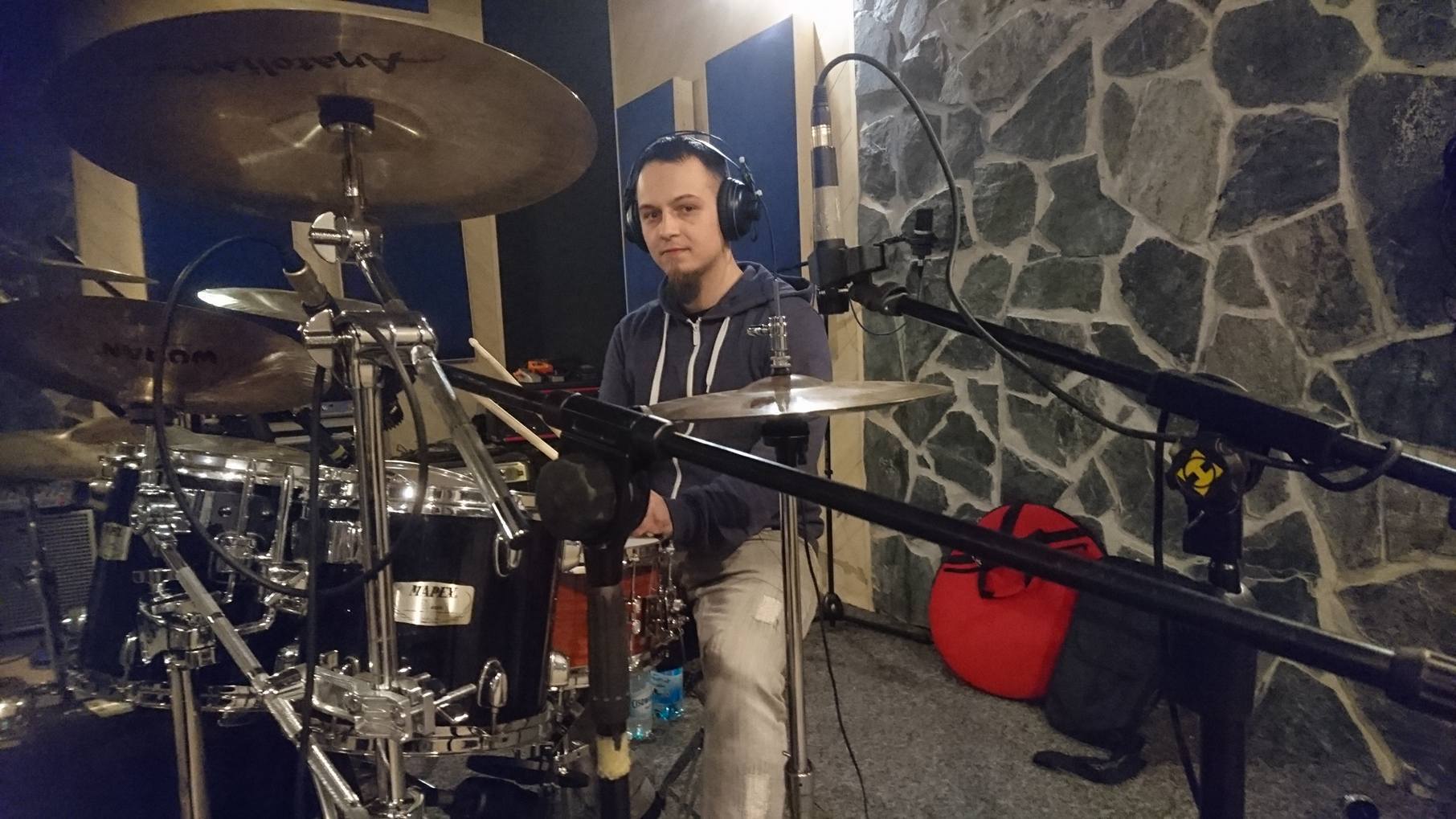 Perkusista z Czechowic-Dziedzic w słuchawkach, grający na perkusji w studiu nagraniowym z kamienną ścianą w tle.