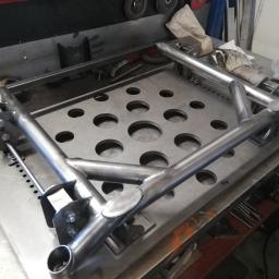 Sky-Welds - Metalowa rama konstrukcyjna z rur, spawana i skręcana śrubami, leżąca na perforowanym stole warsztatowym.