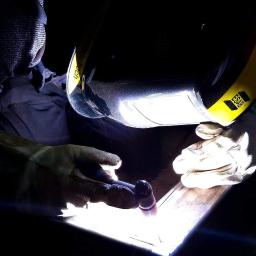 Sky-Welds - Pracownik w hełmie spawalniczym ESAB łączy metalowe elementy metodą TIG, widoczny błysk spawu i elektroda wolframowa.