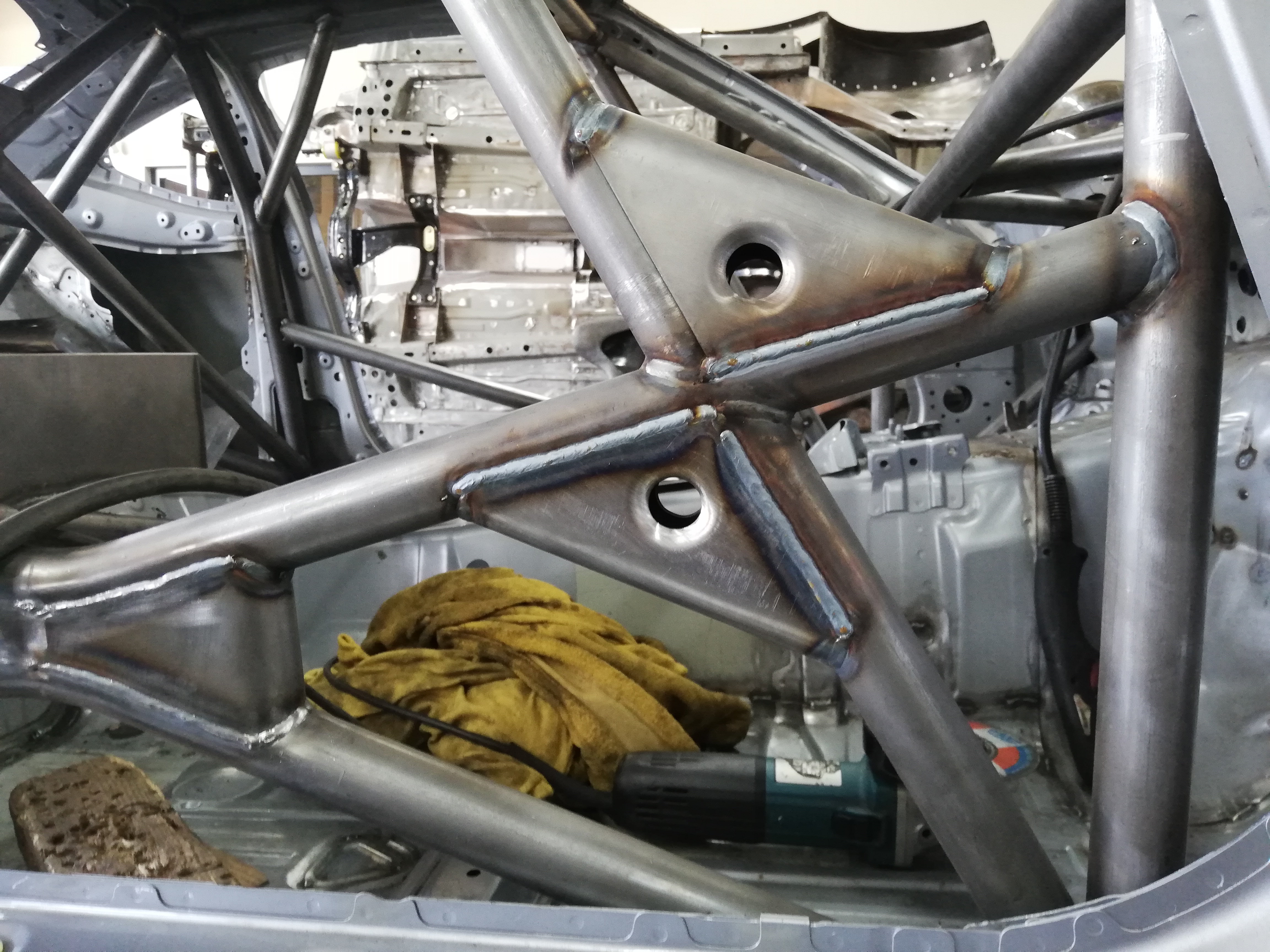 Wnętrze karoserii samochodu z zamontowaną, pospawaną klatką bezpieczeństwa z rur stalowych, widoczne spawy i otwory w konstrukcji.