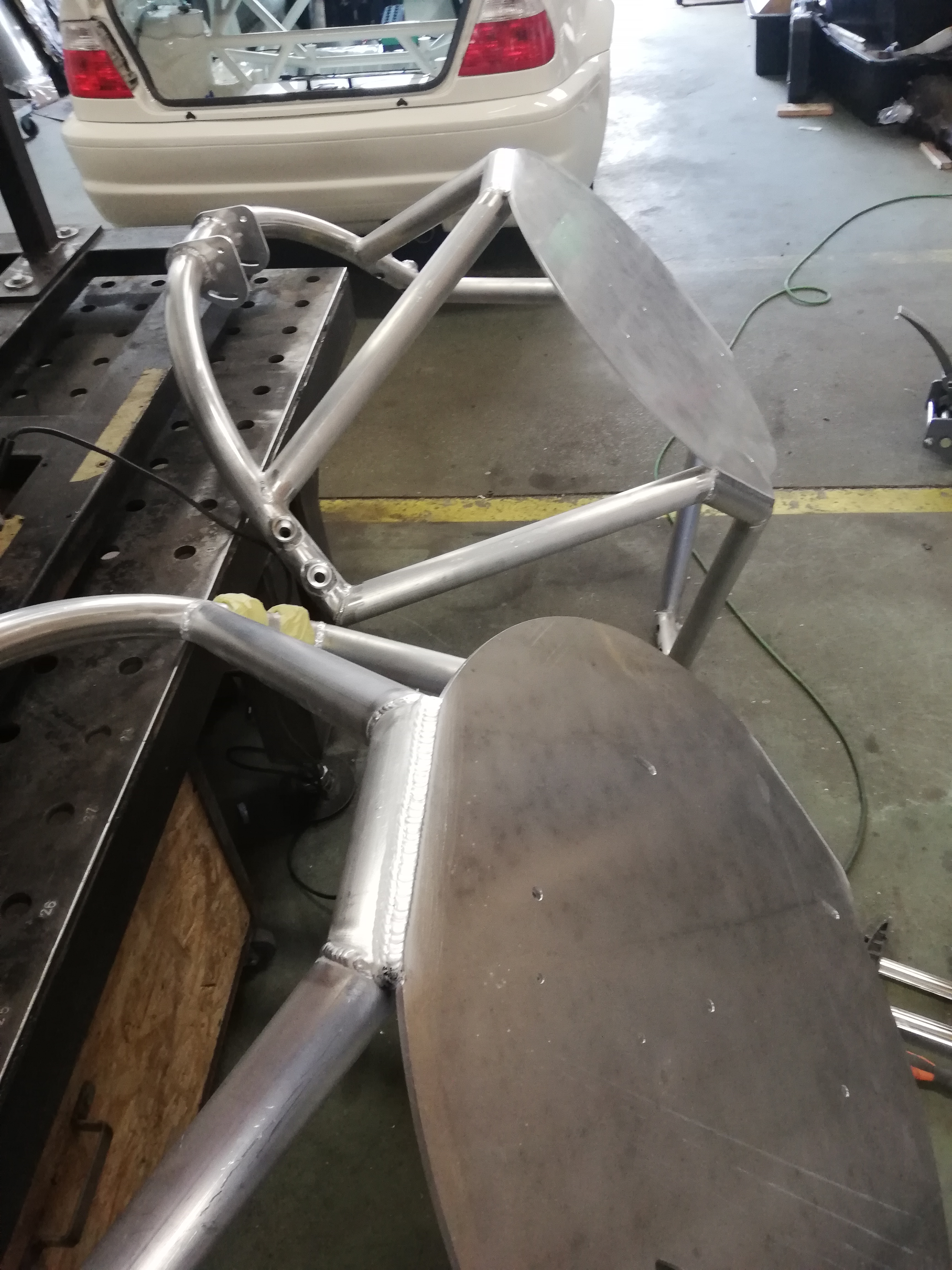 Elementy klatki bezpieczeństwa do samochodu, wykonane z rur i blach, z widocznymi spawami, leżące na stole warsztatowym w trakcie budowy.