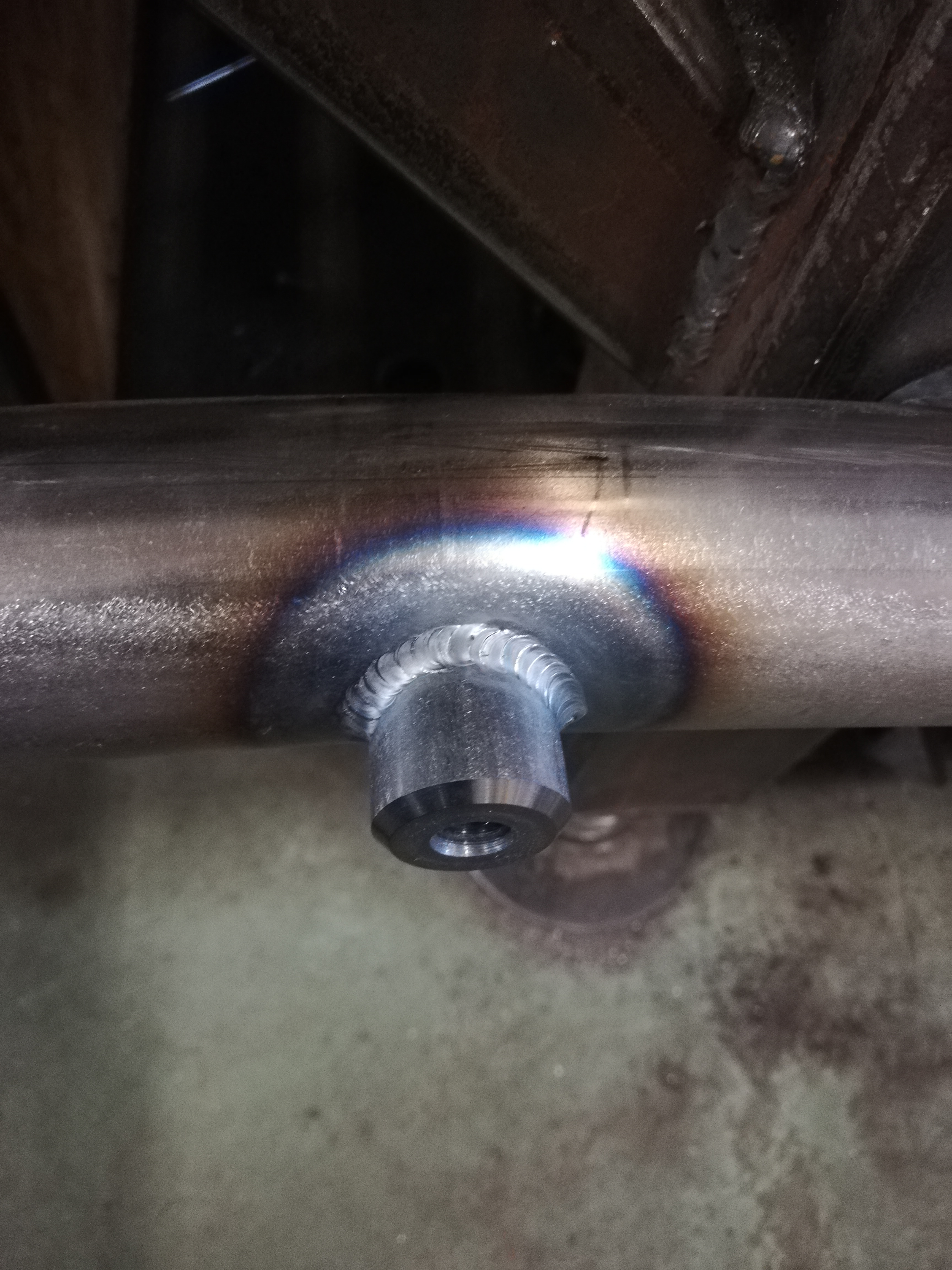 Metalowa rura z przyspawanym elementem z otworem, widoczne ślady po spawaniu i przebarwienia termiczne.