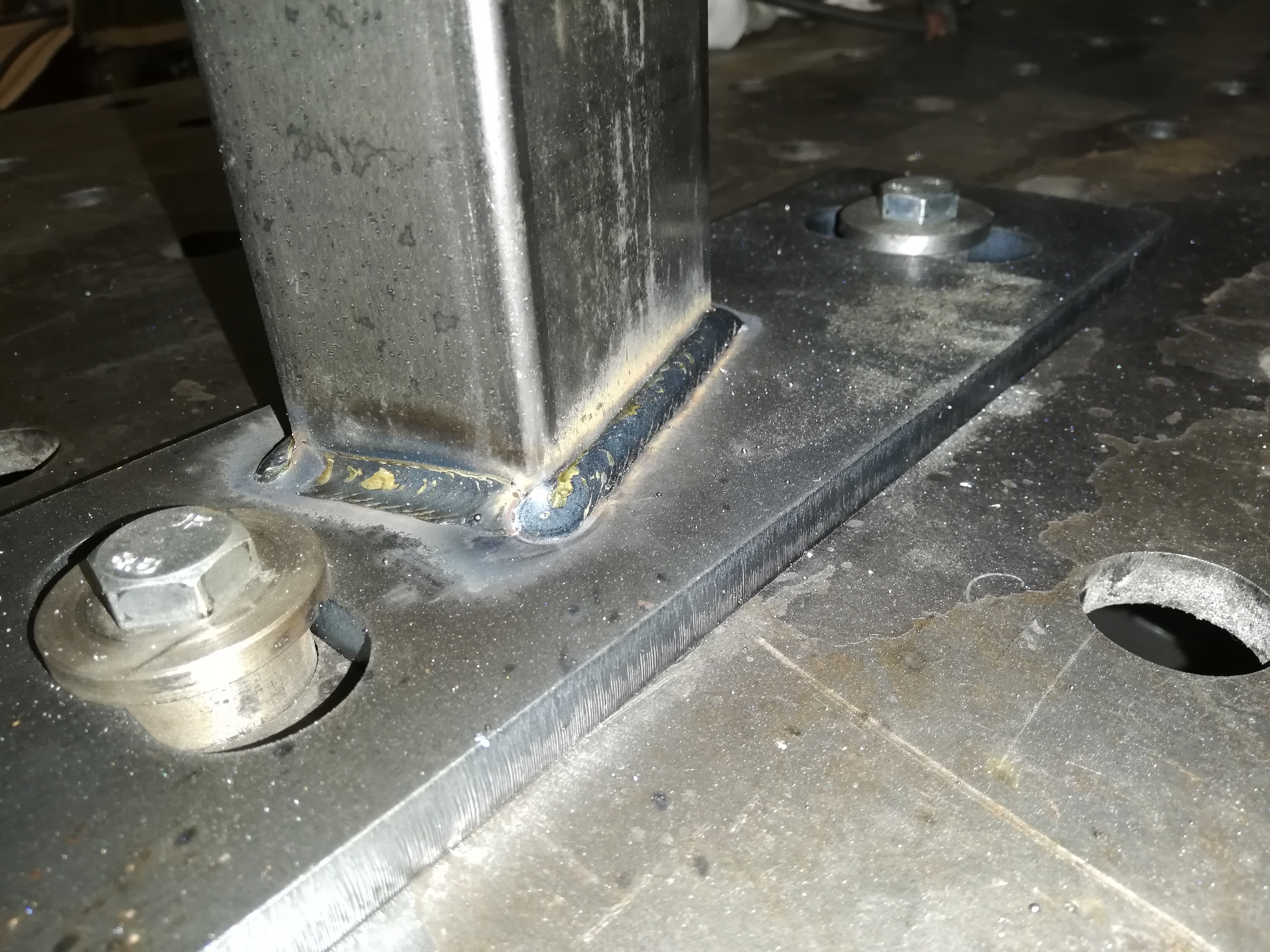 Połączenie spawane rury kwadratowej do metalowej płyty z widocznymi śladami po spawaniu i elementami mocującymi.