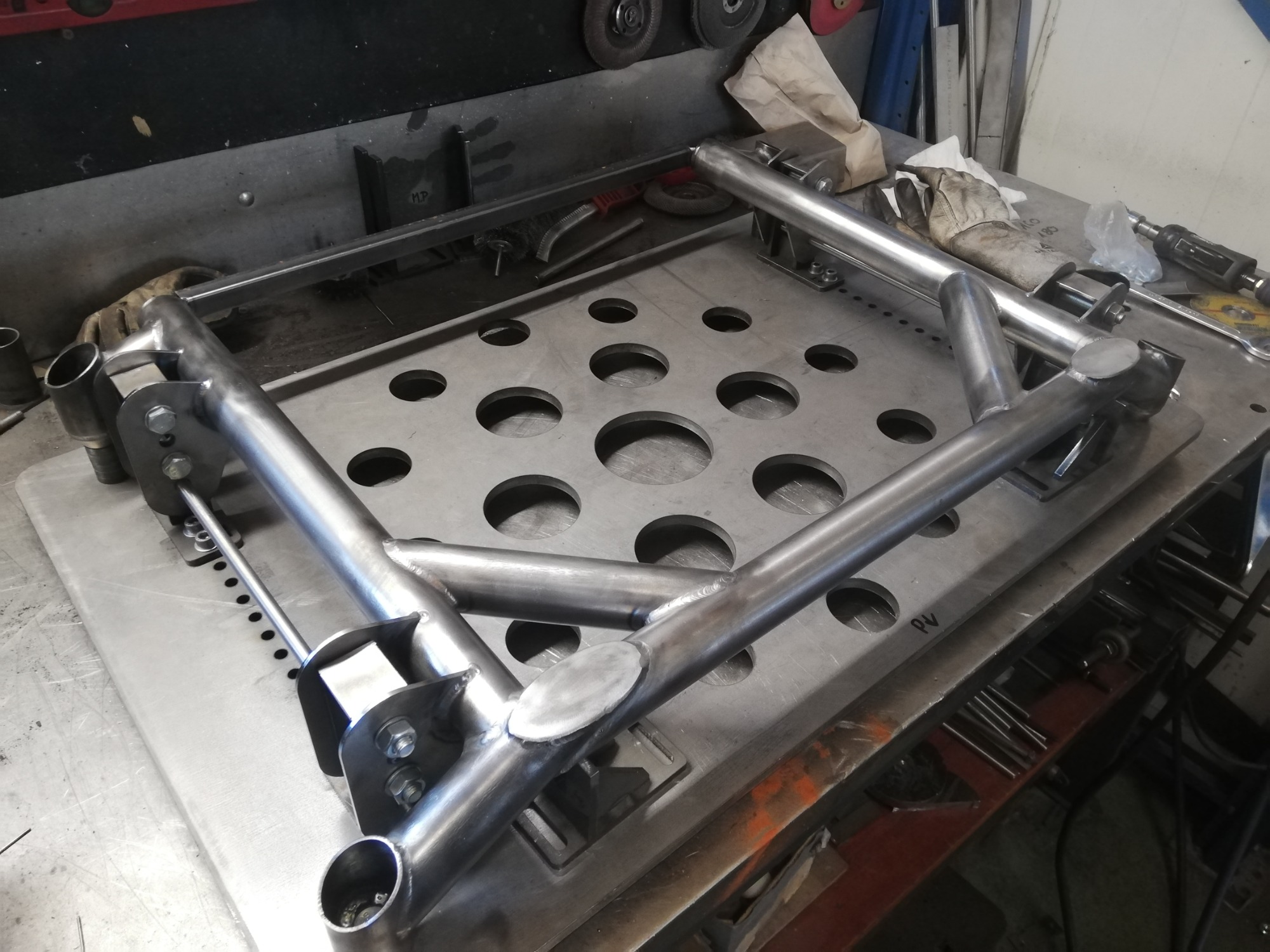 Metalowa rama konstrukcyjna z rur, spawana i skręcana śrubami, leżąca na perforowanym stole warsztatowym.