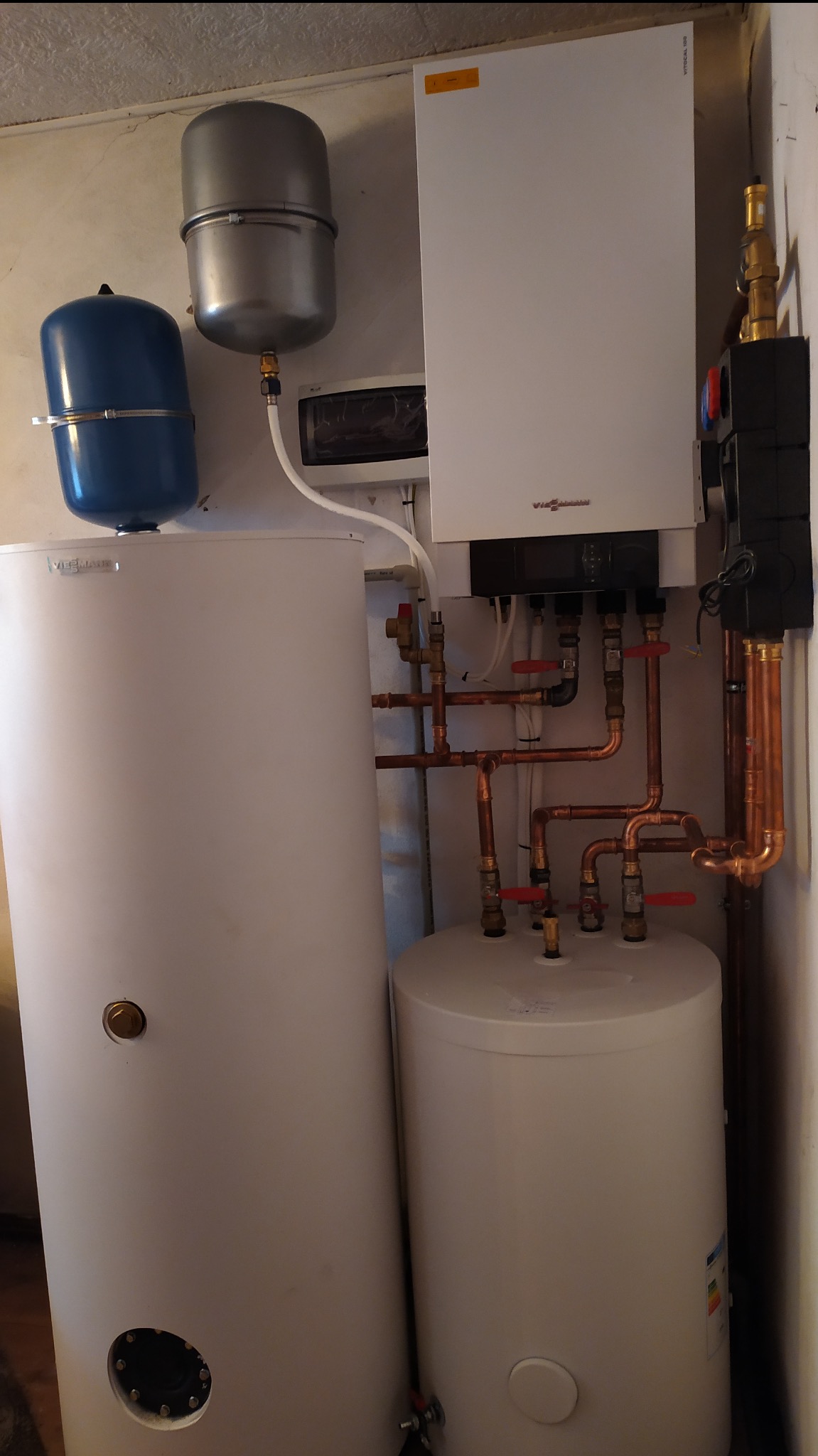 Biały piec gazowy Viessmann z zbiornikami i miedzianymi rurami instalacji CO, zamontowany na ścianie. Widoczne elementy instalacji i zawory.