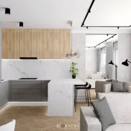 Wnętrze otwartej kuchni z wyspą i salonem, jasne drewno i marmur, czarne akcenty oświetleniowe, parkiet w jodełkę, widok na taras przez okno.