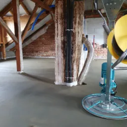 Wyrównywanie świeżo wylanej posadzki w pomieszczeniu na poddaszu z widoczną konstrukcją dachu i maszyną do zacierania.