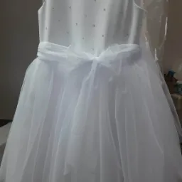 Biała sukienka wizytowa dla dziewczynki, z kr&oacute;tkimi rękawkami i tiulowym dołem, zdobiona drobnymi kryształkami na gorsecie, wisząca na wieszaku.