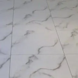 Białe płytki podłogowe imitujące marmur z wyraźnym wzorem żyłkowania, ułożone w regularny wzór z widocznymi fugami. Perspektywa z góry.