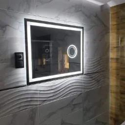 Nowoczesna łazienka z podświetlanym lustrem w ramie, marmurowe płytki z falistym wzorem, drewniane panele po prawej stronie i czarny włącznik światła.