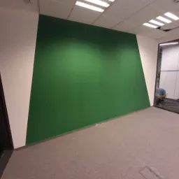 Świeżo pomalowana ściana w biurze na kolor zielony, z białymi akcentami, widoczny pracownik w tle przez szklane drzwi.